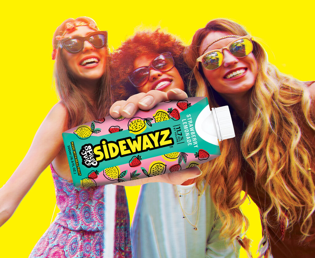 Three smiling young women wearing sunglasses and flower headbands pose together against a bright yellow background, holding a colorful carton labeled “Sidewayz Strawberry Lemonade.”.