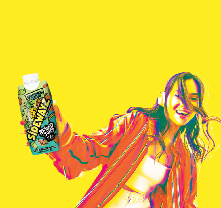A smiling woman in headphones and a bright jacket holds a pineapple-flavored Sidewaiz drink carton against a vibrant yellow background.