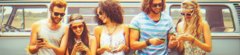 Five young adults in casual, colorful summer outfits stand in front of a retro van, smiling and looking at their phones. They appear relaxed and happy, with a sunny outdoor setting in the background.